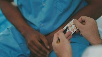 Senior doctor and young male patient who lie on the bed while checking pulse, consult and explain with nurse taking note and supporting in hospital wards. video