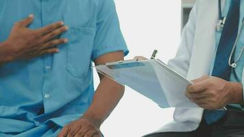 Senior doctor and young male patient who lie on the bed while checking pulse, consult and explain with nurse taking note and supporting in hospital wards. video