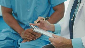 Senior doctor and young male patient who lie on the bed while checking pulse, consult and explain with nurse taking note and supporting in hospital wards. video