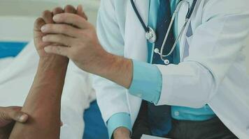 Senior doctor and young male patient who lie on the bed while checking pulse, consult and explain with nurse taking note and supporting in hospital wards. video