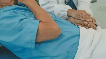 Senior doctor and young male patient who lie on the bed while checking pulse, consult and explain with nurse taking note and supporting in hospital wards. video