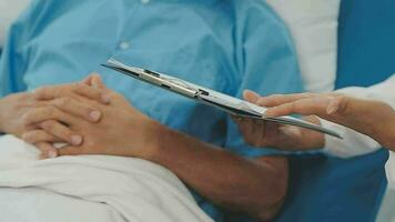 Senior doctor and young male patient who lie on the bed while checking pulse, consult and explain with nurse taking note and supporting in hospital wards. video