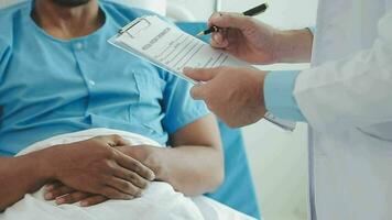 Senior doctor and young male patient who lie on the bed while checking pulse, consult and explain with nurse taking note and supporting in hospital wards. video