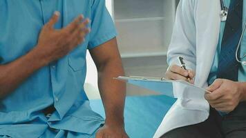 Senior doctor and young male patient who lie on the bed while checking pulse, consult and explain with nurse taking note and supporting in hospital wards. video