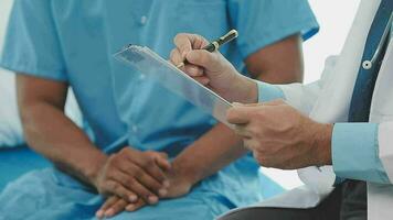 Senior doctor and young male patient who lie on the bed while checking pulse, consult and explain with nurse taking note and supporting in hospital wards. video