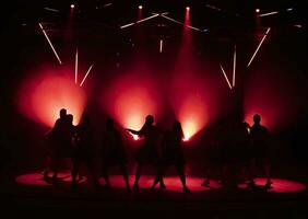 Dark silhouettes of dancing girls against the background of red light from stage spotlights. photo