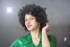 Excited woman in an afro wig on a gray background. Disco girl. photo