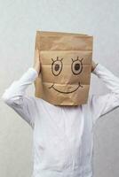 The boy has a cardboard box above his head with a funny smiley face drawn on it. photo