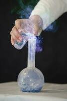 Chemist laboratory assistant pours a luminous mystical solution into a medical flask. photo