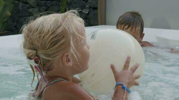 Day is full of fun. Brother with little sister playing ball in hot tub video