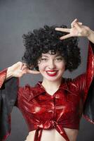 A beautiful girl in a red disco costume and a black curly wig smiles. photo