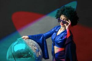 un mujer con un disco pelota en un afro peluca en multicolor rayos de ligero. disco estilo desde el setenta o años ochenta foto