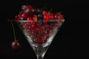 Summer berries in a glass glass on a dark background close-up. photo