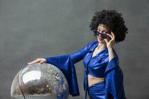 Girl with a disco ball in an afro wig on a gray background. Disco style from the seventies or eighties. photo