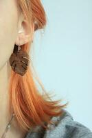 Red haired girl with Craft Wooden earring. Photography of Jewelry. Boho or Rustic Monstera leaf dangles. Redhead hairstyle model. Natural Beauty and eco concept. photo