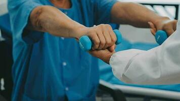 réhabilitation de désactivée gens concept. Jeune physiothérapeute portion Sénior Masculin patient dans fauteuil roulant exercice à maison. handicapé personnes âgées homme formation avec haltères video