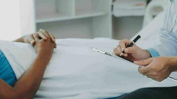 Doctor and patient sitting and talking at medical examination at hospital office, close-up. Therapist filling up medication history records. Medicine and healthcare concept. video