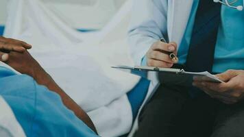 Doctor and patient sitting and talking at medical examination at hospital office, close-up. Therapist filling up medication history records. Medicine and healthcare concept. video