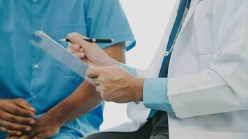 Doctor and patient sitting and talking at medical examination at hospital office, close-up. Therapist filling up medication history records. Medicine and healthcare concept. video