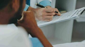 Doctor and patient sitting and talking at medical examination at hospital office, close-up. Therapist filling up medication history records. Medicine and healthcare concept. video