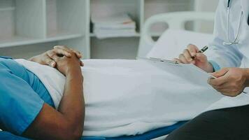 Doctor and patient sitting and talking at medical examination at hospital office, close-up. Therapist filling up medication history records. Medicine and healthcare concept. video