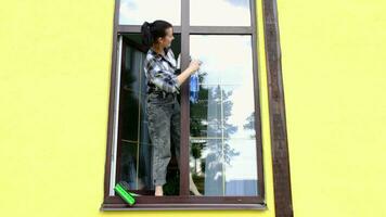 A woman manually washes the window of the house with a rag with a spray cleaner and a mop outside. Safety at height, restoring order and cleanliness in the spring, cleaning service video