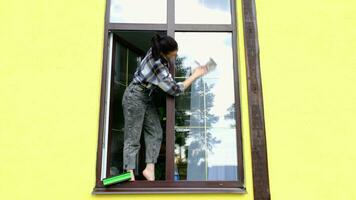 ein Frau manuell wäscht das Fenster von das Haus mit ein Lappen mit ein sprühen Reiniger und ein Mopp außen. Sicherheit beim Höhe, Wiederherstellen bestellen und Sauberkeit im das Frühling, Reinigung Bedienung video