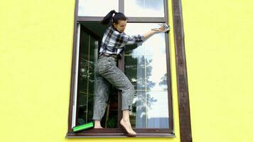 A woman manually washes the window of the house with a rag with a spray cleaner and a mop outside. Safety at height, restoring order and cleanliness in the spring, cleaning service video