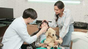 asiático masculino pediátrico dentista cheques y examina muchachas dientes con su madre alentado en dental clínica, bienestar higiene, y profesional ortodoncia cuidado de la salud trabajo en niño y familia hospital. video