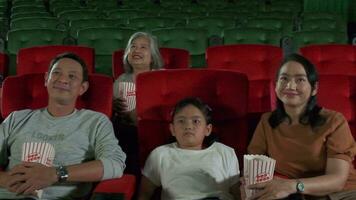 asiatico famiglia pubblico godere Guardando cinema insieme a film teatri. ragazzo e genitori avere interno divertimento stile di vita con prestazione film arte mostrare, contento e allegro con Popcorn e Sorridi. video