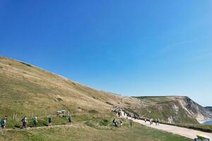 High Angle View of People are Approaching to Durdle Door Beach Which is Most Famous Tourist Attraction Place Through Walking Distance over Landscape and Hills. Captured on September 9th, 2023 photo