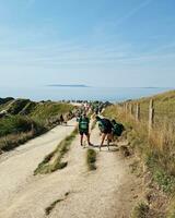 alto ángulo ver de personas son que se acerca a durdle puerta playa cuales es más famoso turista atracción sitio mediante caminando distancia terminado paisaje y sierras. capturado en septiembre 9, 2023 foto