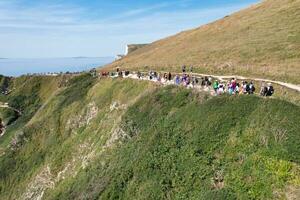 High Angle View of People are Approaching to Durdle Door Beach Which is Most Famous Tourist Attraction Place Through Walking Distance over Landscape and Hills. Captured on September 9th, 2023 photo