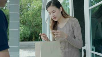 Happy smiling Asian woman receives paper bag parcel of food from courier front house. Delivery man send deliver express. online shopping, paper container, takeaway, postman, delivery service, packages video