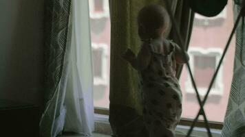 A baby girl in an overall playing with curtains near the large window video