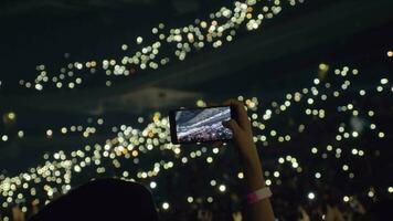 Audience with lights in concert hall and woman taking mobile video