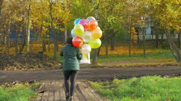 un camara lenta de un mujer caminando con globos en un hermosa otoño día video