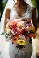Macro shot of a brides intricate lace gown gripping her vibrant colorful wedding bouquet photo