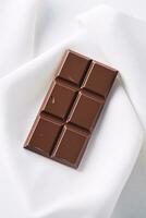 Smooth Glossy Chocolate Bar Resting on White Linen Backdrop with Copyspace Right AI Generative photo