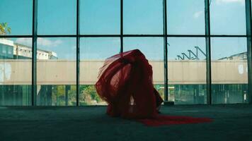 un asiático hombre bailando con un rojo paño cubierta su cuerpo en frente de un edificio ventana video