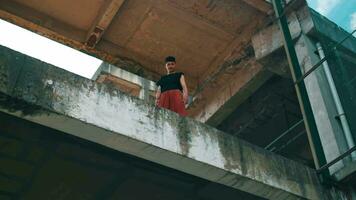 an Asian man standing on the concrete edge of a building looking down from a high elevation video