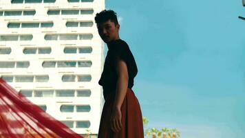 an Asian man standing in front of a building with a blue sky and red cloth flying video