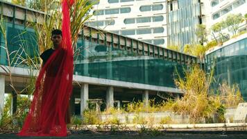 un asiático hombre en pie con un rojo paño envuelto alrededor su cuerpo mientras en frente de un abandonado edificio video