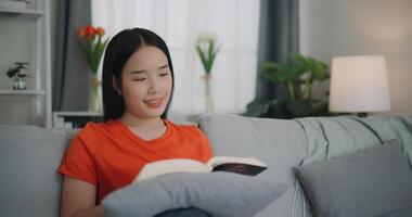 asiático mujer leyendo un libro mientras sentado en el sofá foto