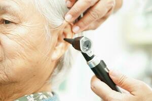 Otolaryngologist or ENT physician doctor examining senior patient ear with otoscope, hearing loss problem. photo