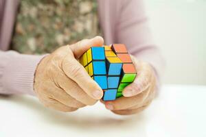 Bangkok, Thailand - May 15, 2022 Asian elderly woman playing Rubik cube game to practice brain training for help dementia prevention and Alzheimer disease. photo