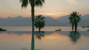 A steadicam shot of a glossy swimming pool boundary and an evening sea landscape on the background video