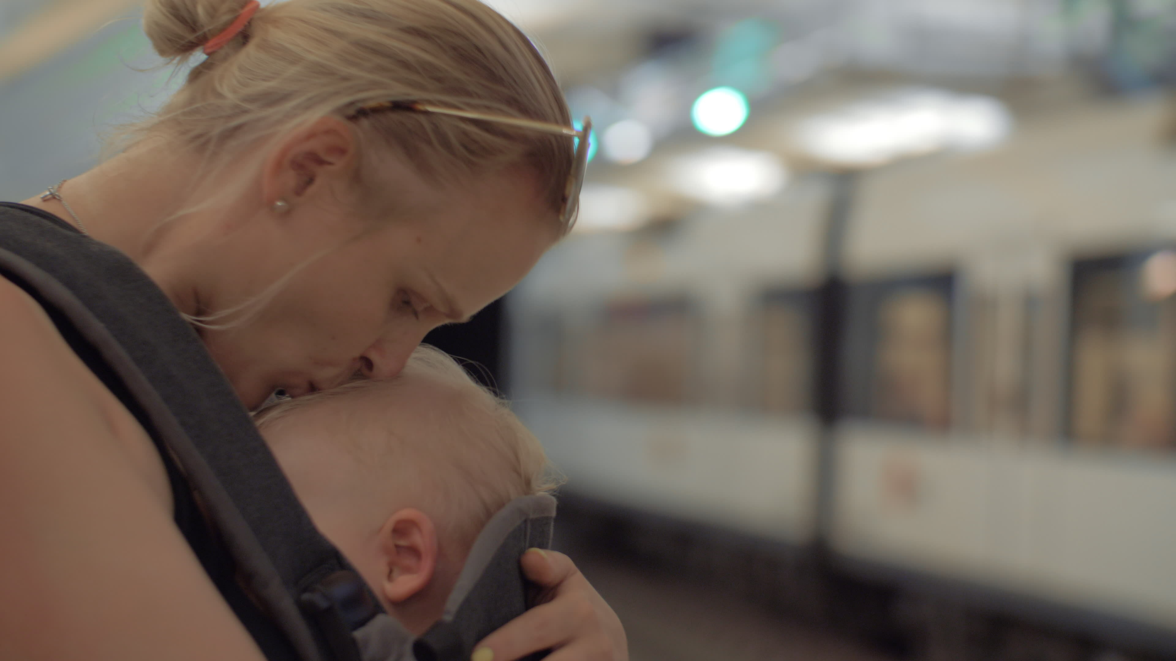 Mum with sleeping child in baby carrier waiting for subway train