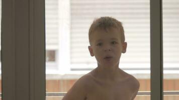 Funny kid fooling with towel and having fun, view through the glass video