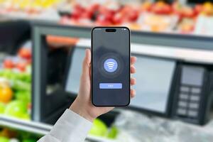 Woman holds a smartphone, displaying an NFC payment. Grocery store market in background. Concept of faster and more efficient shopping with apps photo